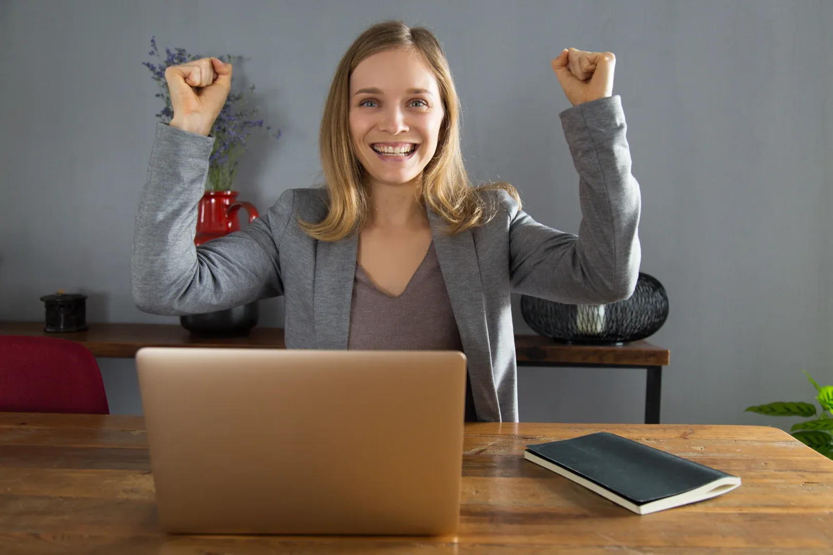 Qual a relação da pós-graduação EaD e mercado de trabalho? | Foto de uma mulher de negócios sentada em uma mesa com o notebook aberto comemorando algo | FAVENI