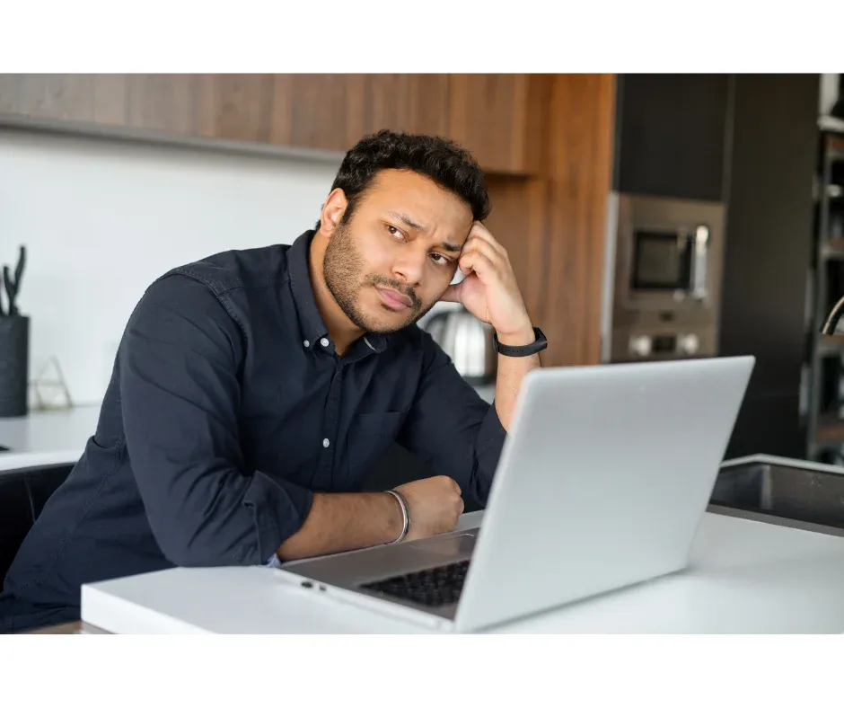 Como o curso de pós-graduação EaD ajuda a mudar de carreira? | Foto de homem indiano em frente ao notebook com uma expressão triste | FAVENI