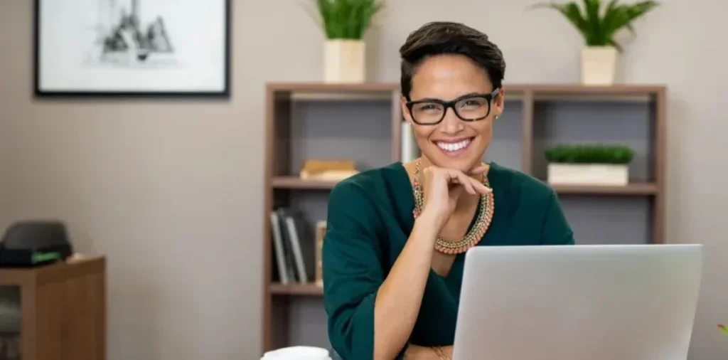 Qual é o papel da pós EaD na requalificação profissional? | Foto de mulher sorrindo para câmera com notebook em sua frente | FAVENI